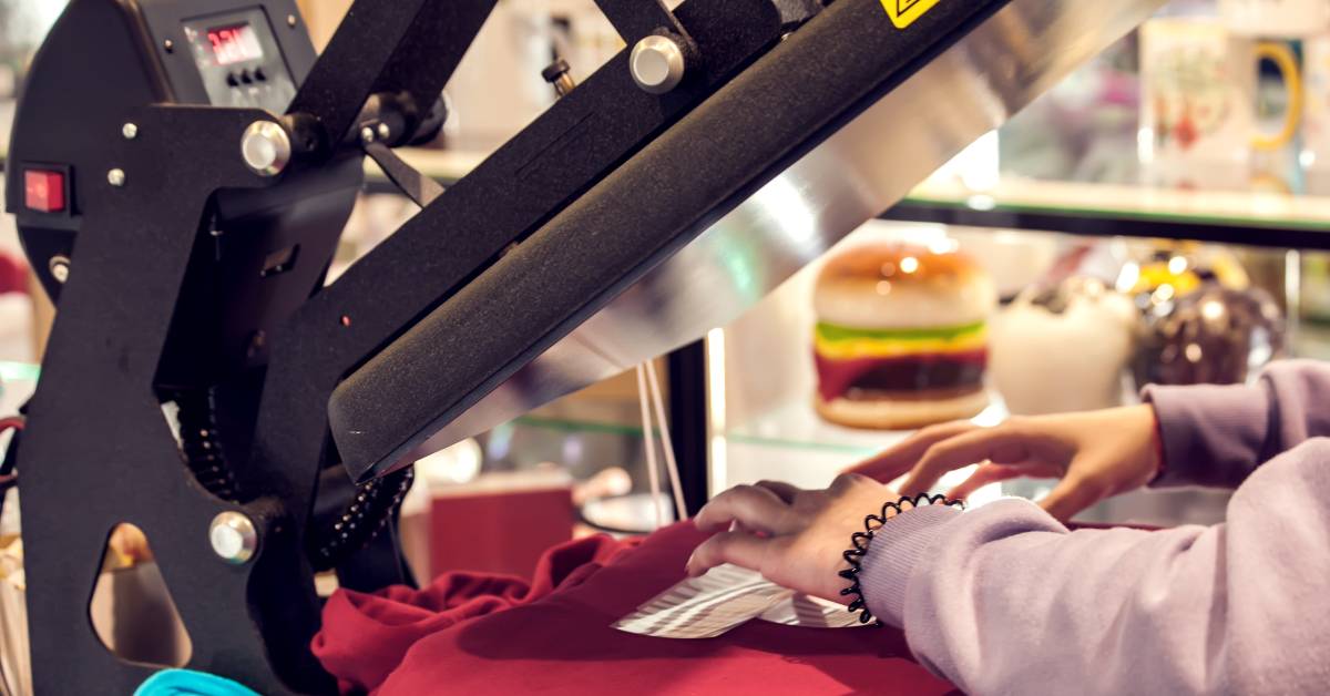 Close-up of a pair of hands straightening out a red sweatshirt onto a T-shirt printing press machine.